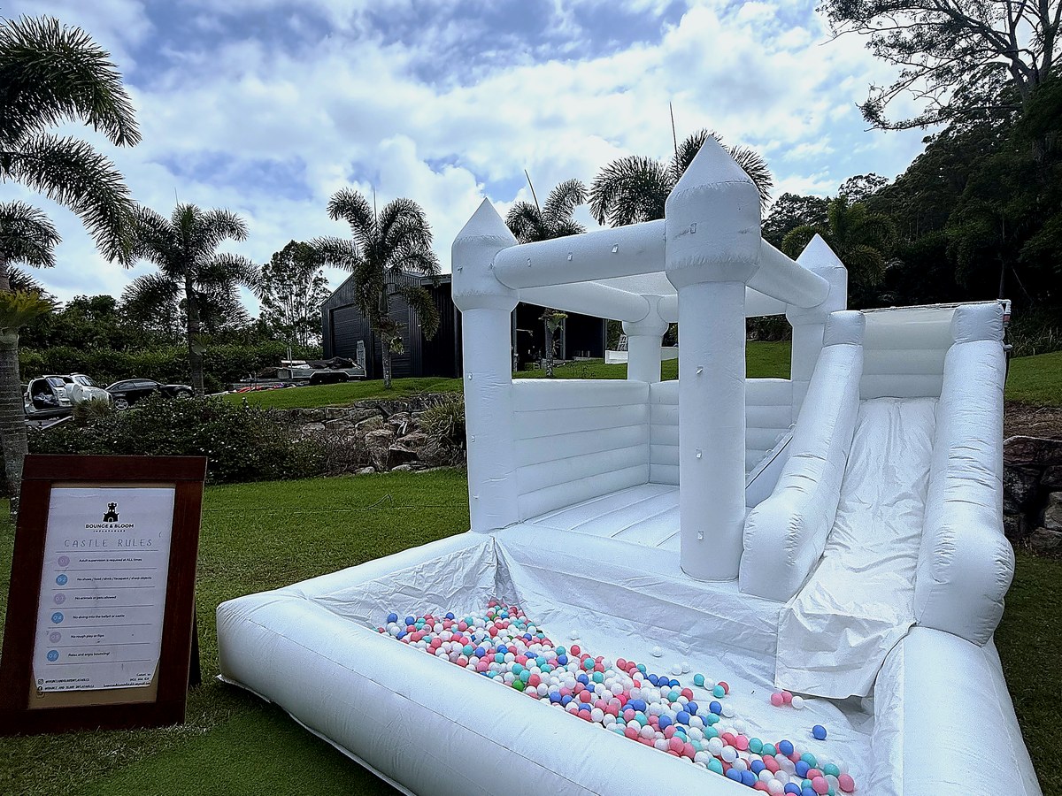 White jumping castle with slide set up on a backyard lawn