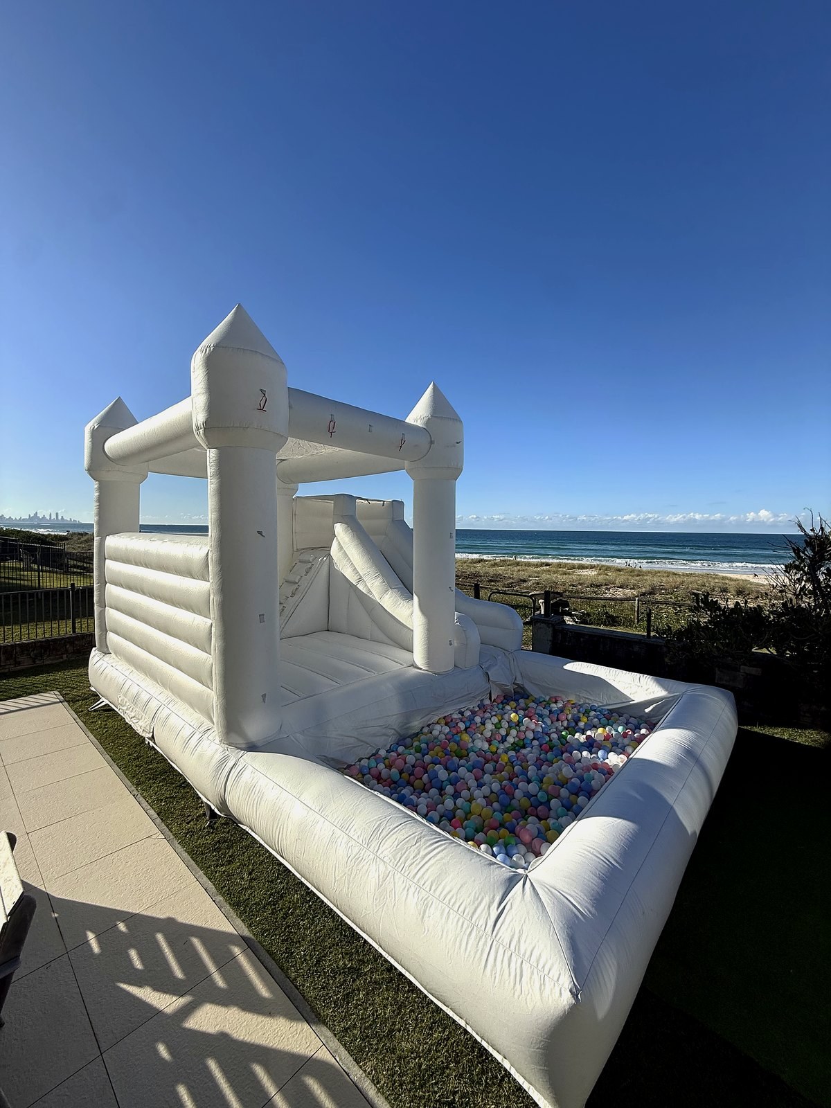 White jumping castle with a ball pit set up on the grass overlooking the beach